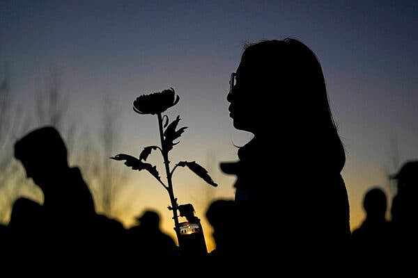 A woman holding a candle and a flower at sunset.