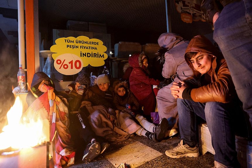 Youngsters sit around a fire near the site of a collapsed hospital, following an earthquake in Iskenderun