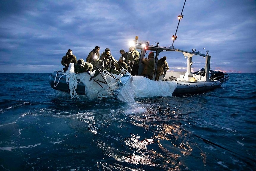 A group of people on a boat on water pulling a large plastic sheet