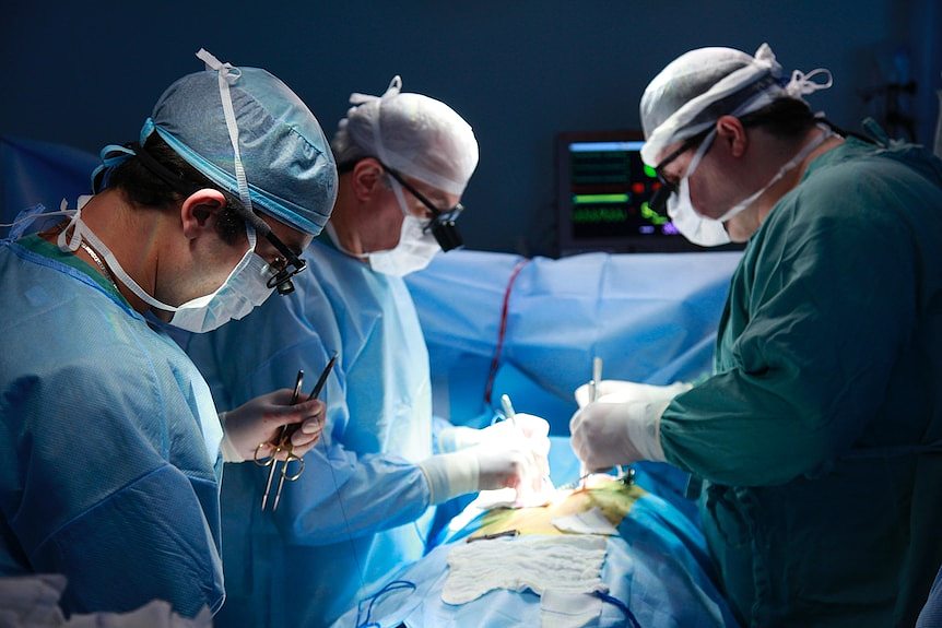 Three surgeons perform a surgical procedure in an operating room.