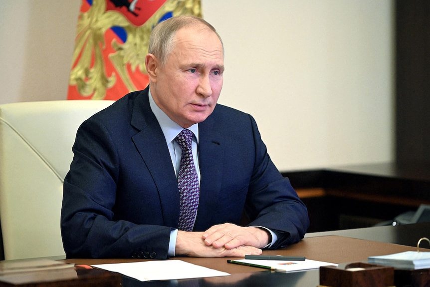 Russian President Vladimir Putin sits at a desk