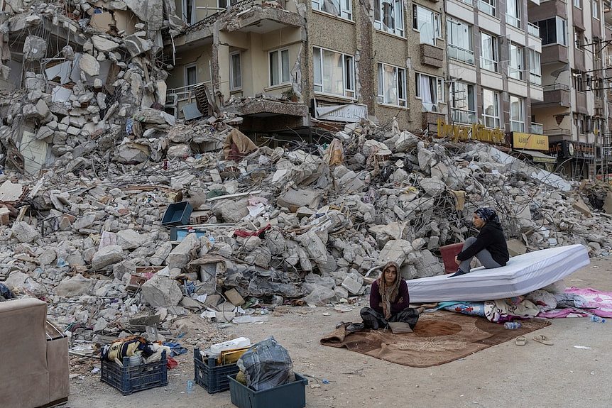 Two people sit outside a destroyed building in Hatay province Türkiye.