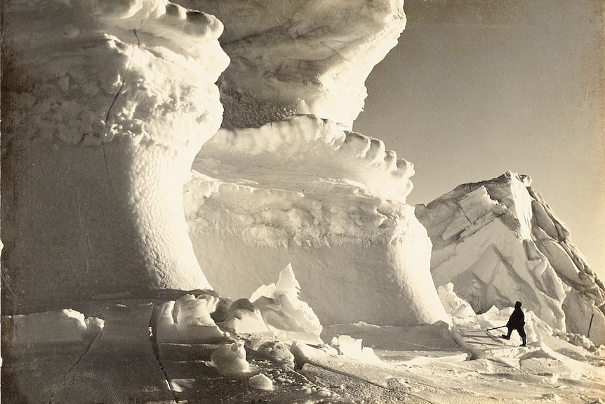 A man in the bottom left of the frame looks up at massive ice cliffs in front of him.