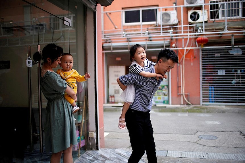 A man and a woman each carry a child as they leave a building. 