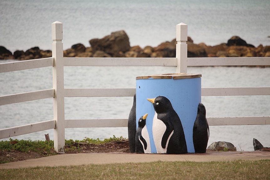 A blue bin with penguins on its side in front of the ocean