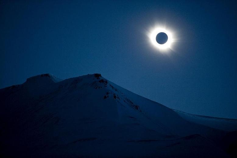 A total solar eclipse is seen next to a snowy mountain