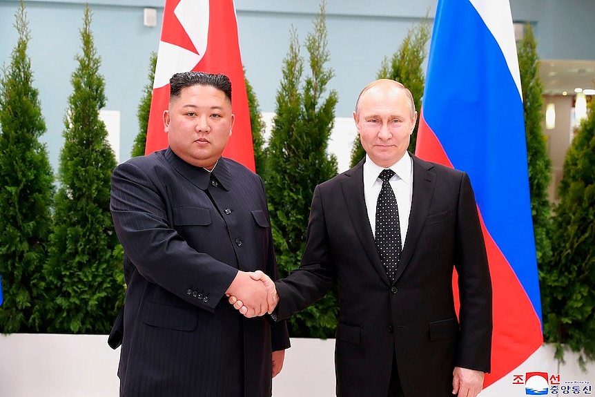 Two men in suits shake hands as the stand in front of North Korean and Russian flags