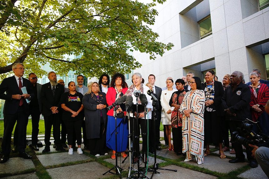 Pat Anderson speaks in a parliament courtyard, surrounded by other advocates and government politicians.