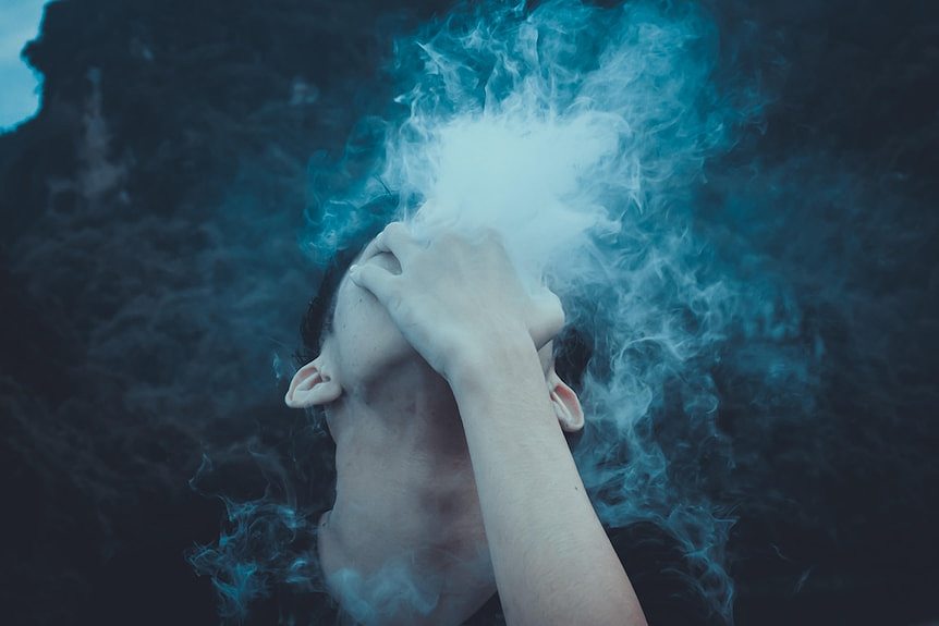 A boy looking up to the sky, holding his hand over his face with vapour coming through his fingers