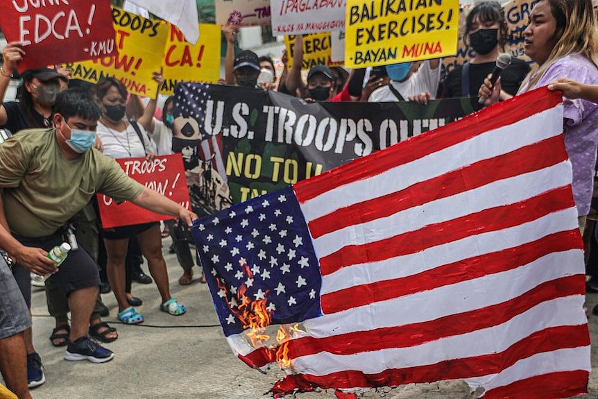 Picture of a group of men and women protesting on a street and burning US flag