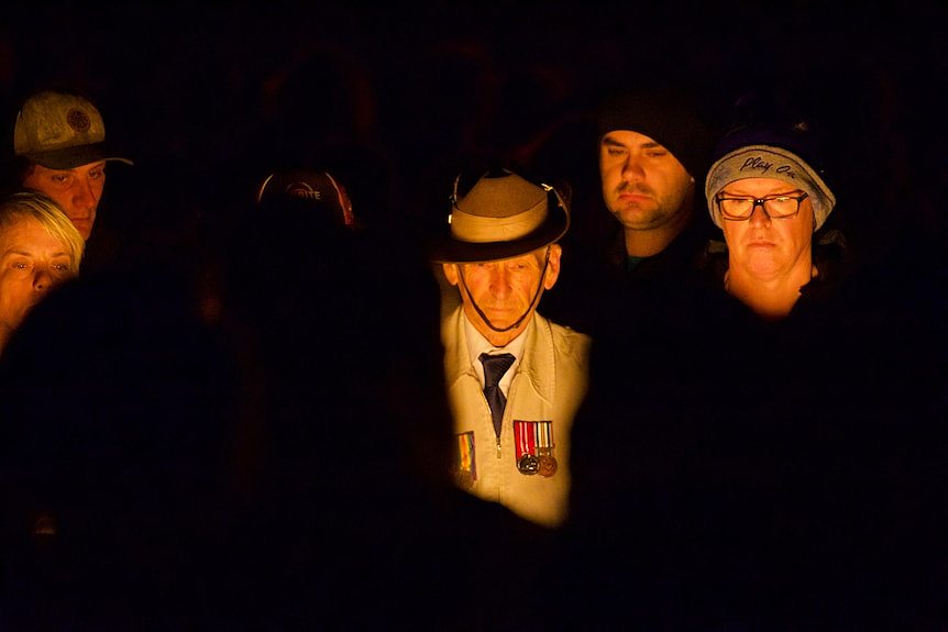 A dark backdrop with a soldier in a crowd.