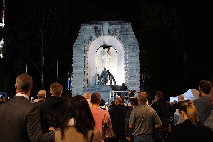 A war memorial structure in Adelaide surrounded by a crowd in the dark.