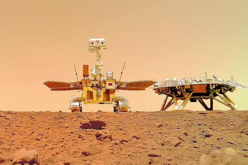 Chinese Mars rover Zhurong sits on the dusty ground near its landing platform bearing a Chinese flag.