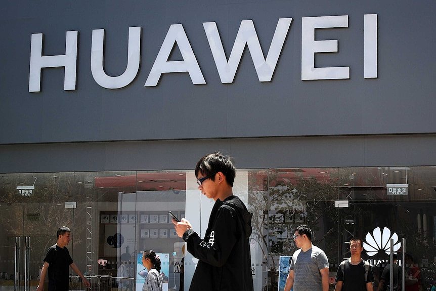 A man looks at his phone as he walks past a Huawei retail store during the day