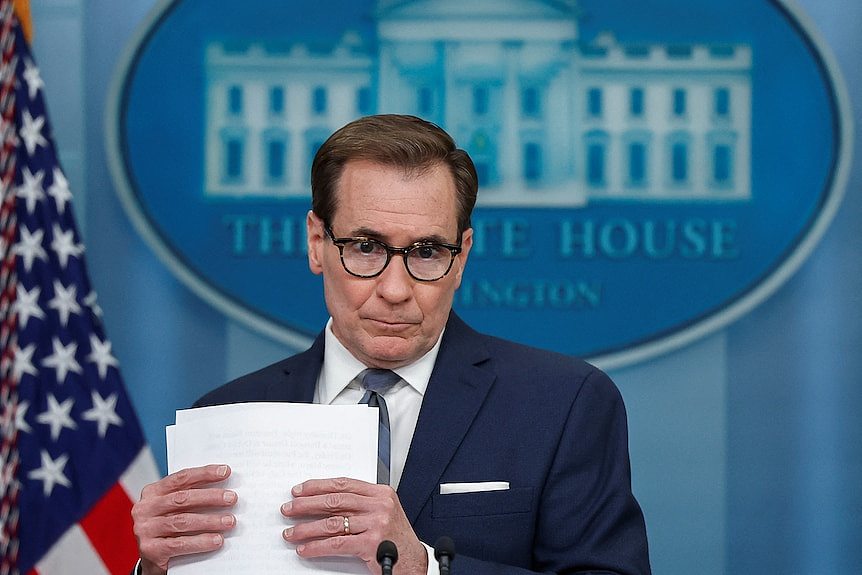 John Kirby shuffles papers at the podium in the white house press briefing room. 