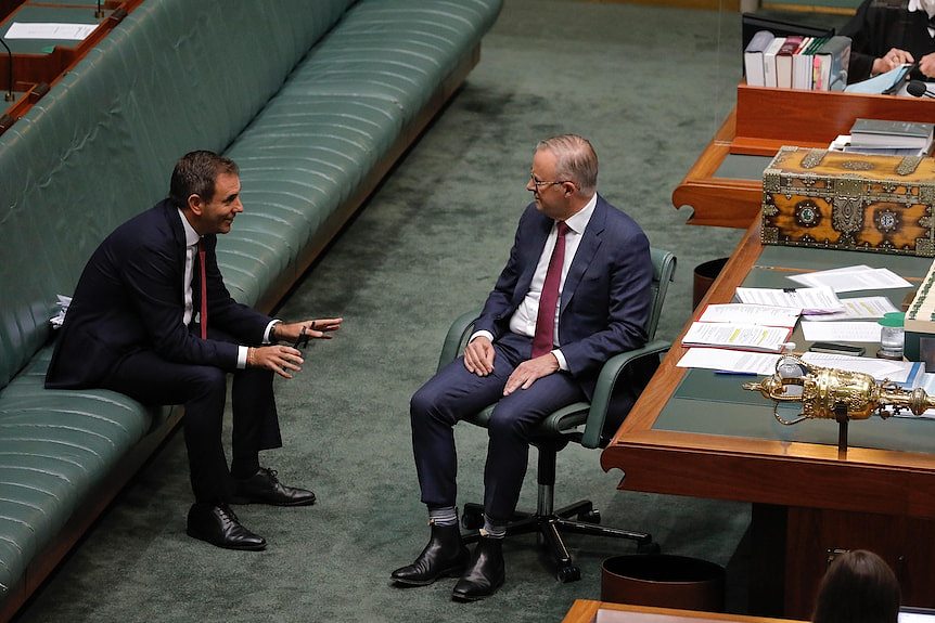 Two middle-aged men in suits sit talking on the government frontbench of the House of Representatives.