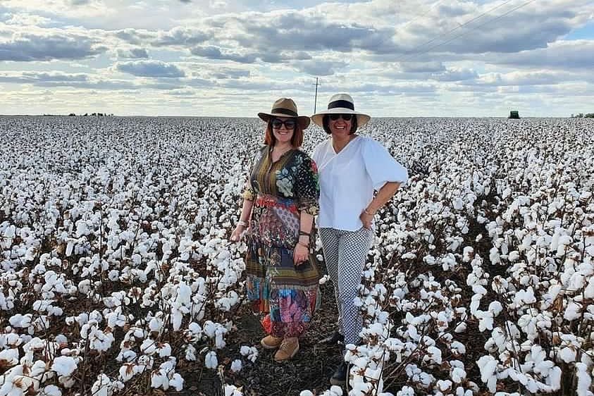 Two women in dresses and hats stand in a cotton field 