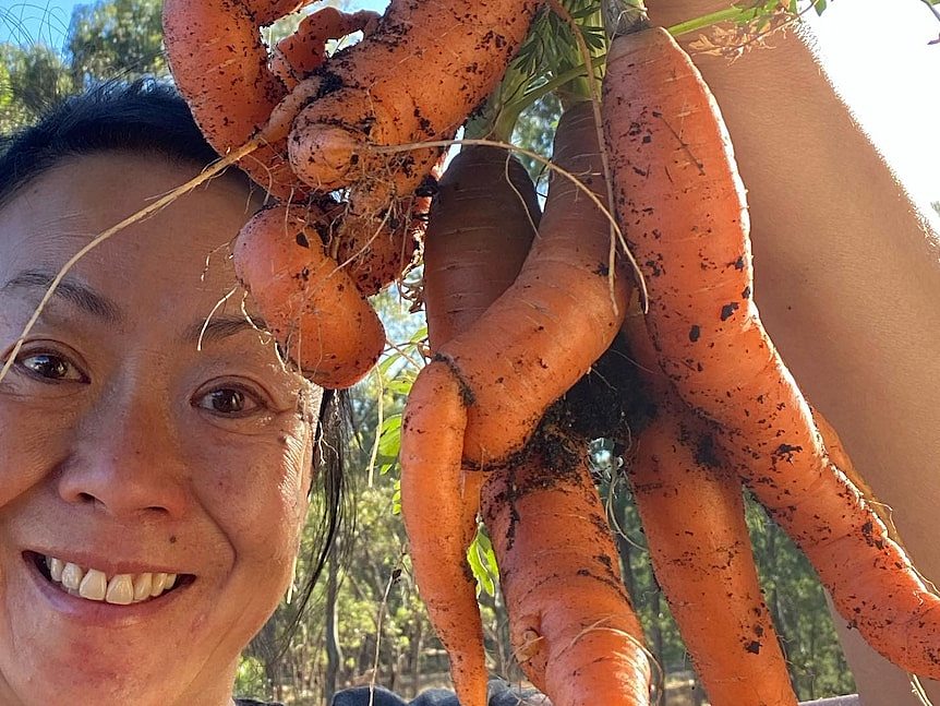 a selfie of a woman with carrots from her vegetable garden 