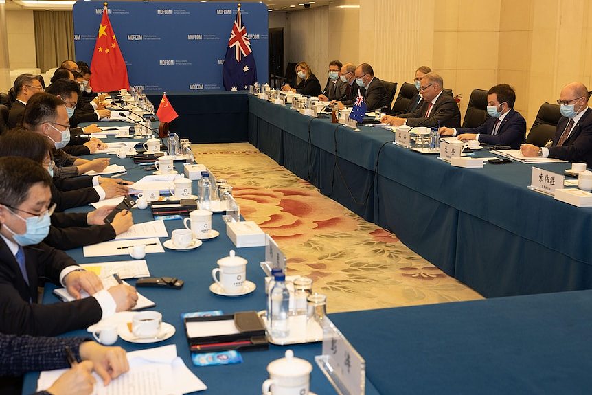 Men in suits seated along two long tables facing each other, with Australian and Chinese flags at end of tables.