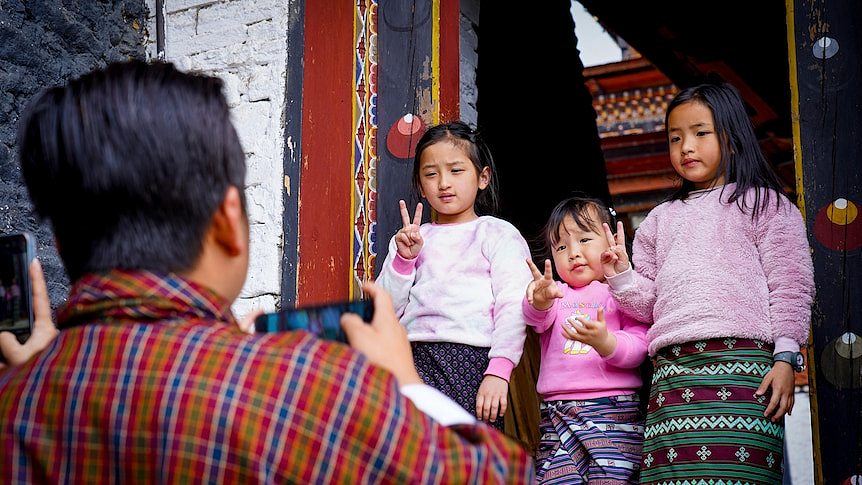 Three little girls give a peace sign while a man takes a photo 