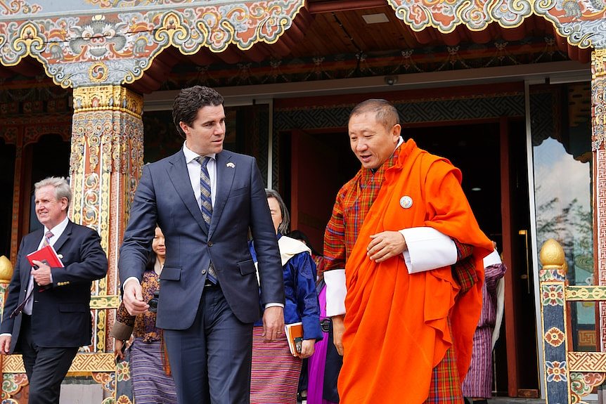 A man in a suit walks with a Bhutanese man in orange robes 