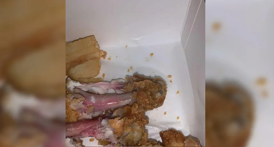 在炸薯条旁边的外卖包装中可以看到肯德基鸡肉，鸡肉呈粉红色，生的。