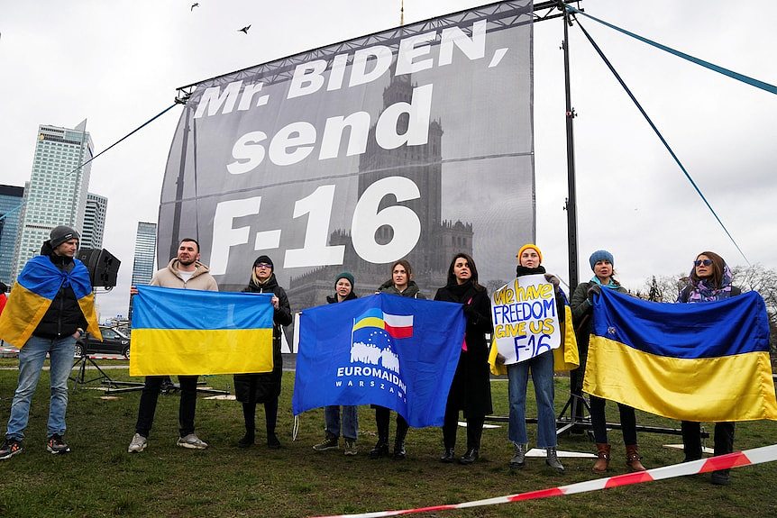 Protesters hold up Ukrainian flags in front of a big sign that reads, 