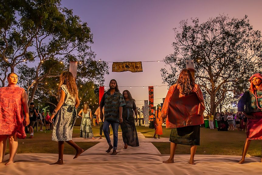 A group of models walk down a runway at an outdoor fashion show