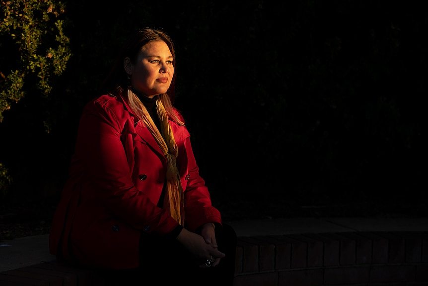 A woman standing in the dark staring off into the distance. 