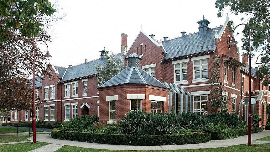一座漂亮的大型维多利亚式红色和奶油色建筑，带有蓝色瓷砖屋顶，坐落在修剪整齐的草坪上。