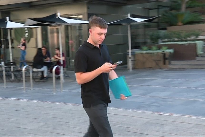 一名身穿 Polo 衫的男子边走边看手机。