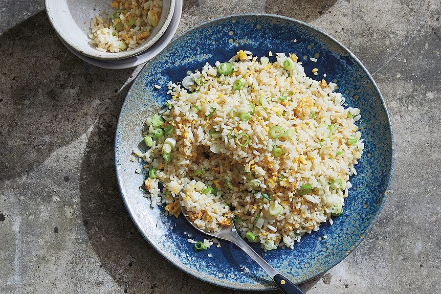 Blue bowl of egg fried rice with a spoon in natural light
