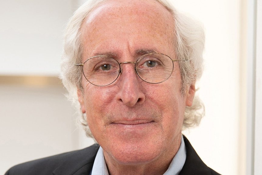 Bruce Wolpe poses for a formal headshot wearing a dark jacket and pale blue shirt