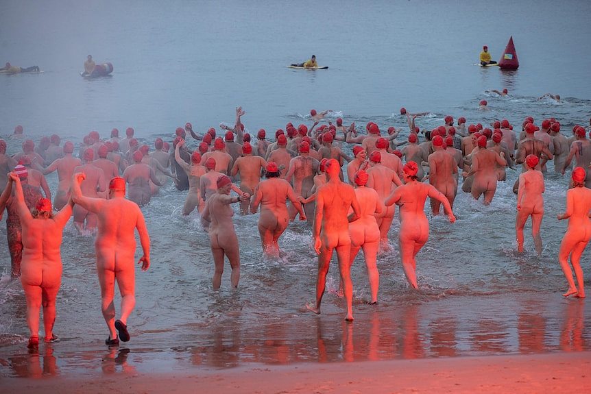 Nude swimmers rush into water en masse.