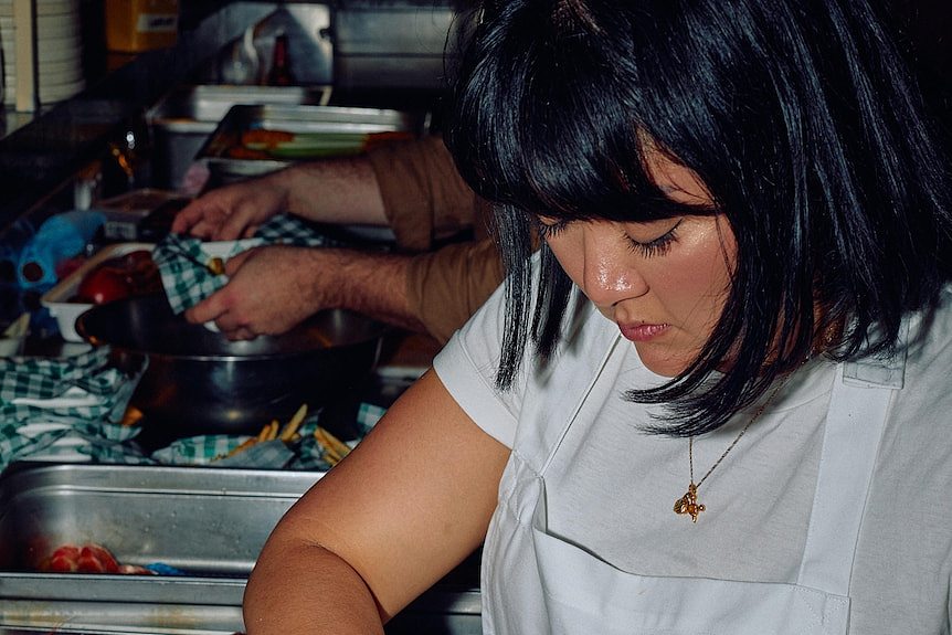 Melbourne chef Rosheen Kaul works with seafood while in a kitchen with staff. She wears a white apron. 