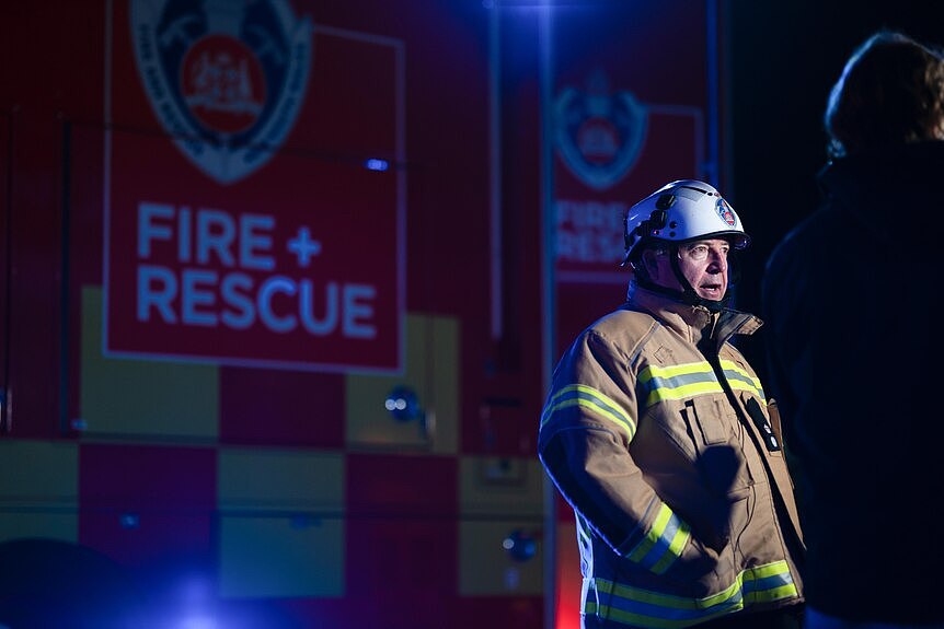 一名身穿防护消防服的男子站在消防救援车前