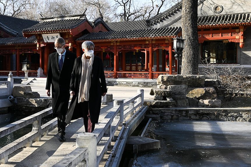 Penny Wong and Graham Fletcher walk across a bridge in front of an ornate Chinese style house. 