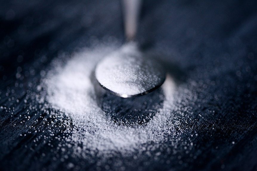 A close up photo of a silver teaspoon piled with white sugar or sweetener