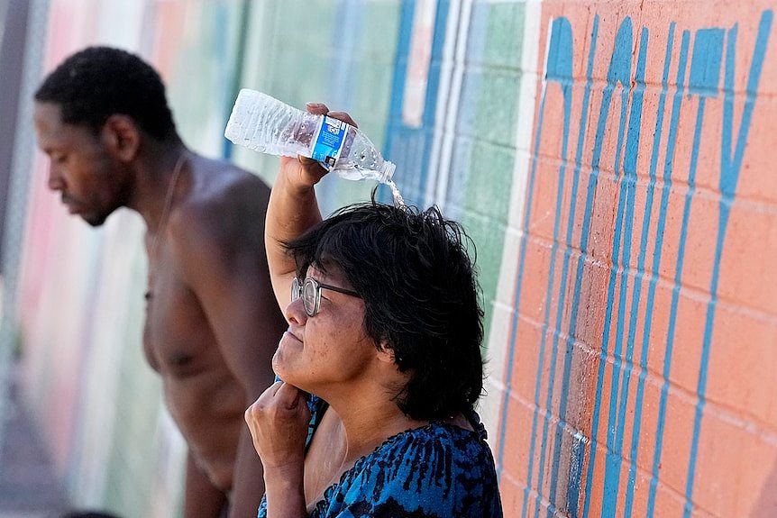 A homeless woman in Phoenix tries to cool down by pouring a bottle of water over her head.