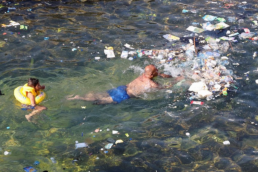 在黎巴嫩首都贝鲁特附近的地中海，人们在漂浮在水面上垃圾旁游泳降暑。