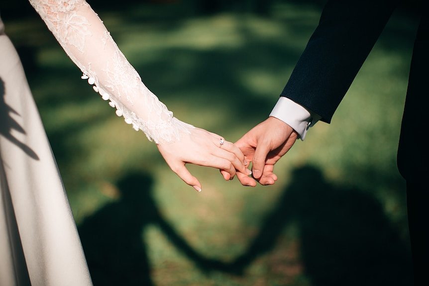 Hand of woman wearing wedding dress holding hand of man wearing suit  