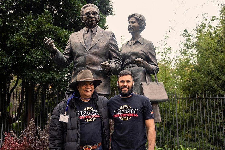 Gary Murray and Djaran Murray-Jackson pose smiling for a photo in front of a statue of Pastor Sir Doug Nicholls and Lady Gladys.