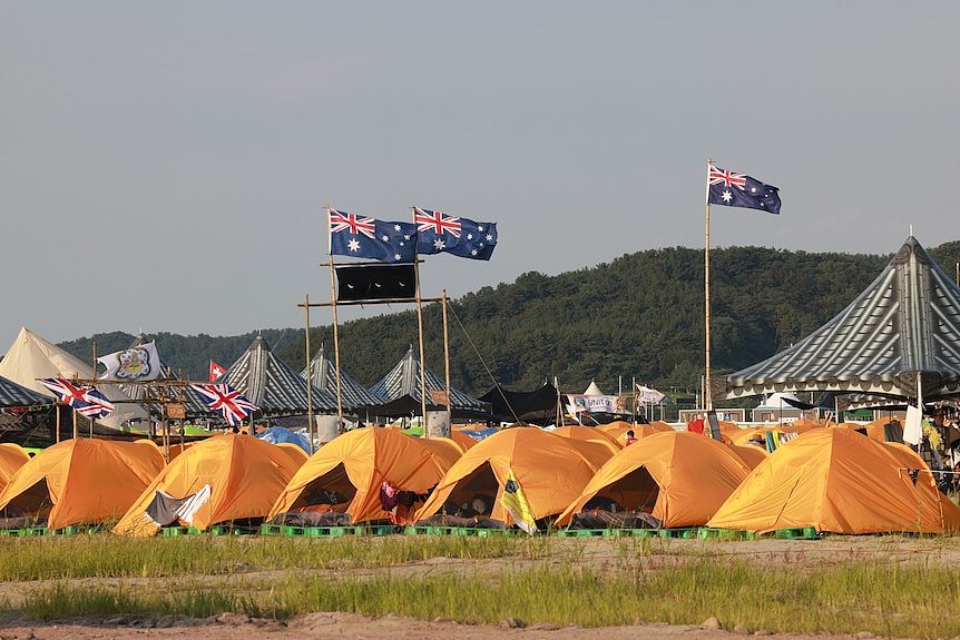 Yellow tents in a line. Three Australian flags fly on poles. 