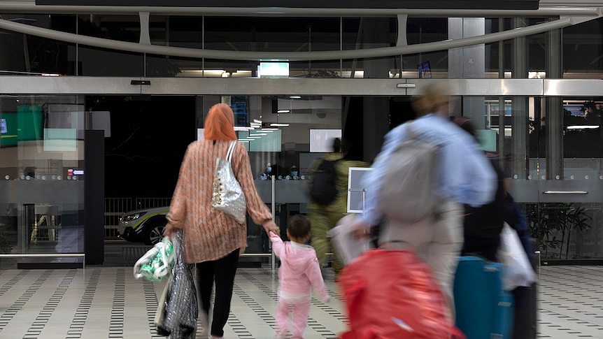 A family carrying luggage walks out the doors of an airport terminal