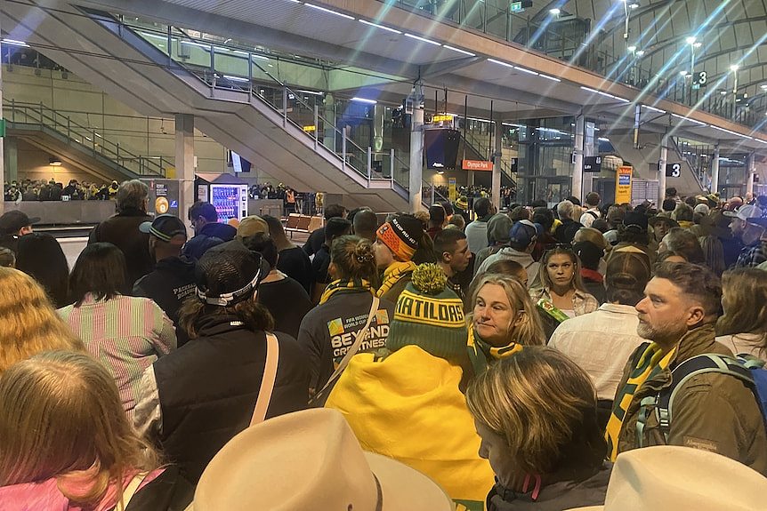 A clsoe up of a crowd of fans in matildas colours waiting at train station 
