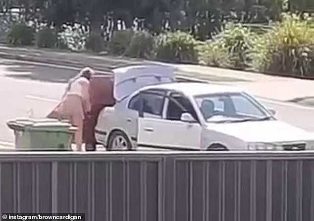 A disturbed man filmed as a female driver used a hand trolley strapped to her car to tow an old cabinet (pictured, the woman inspecting the ratchet straps)