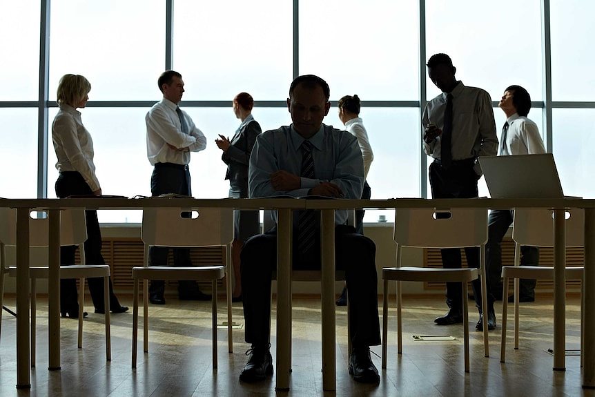 Silhouettes of office workers sitting and standing beside a desk and window.