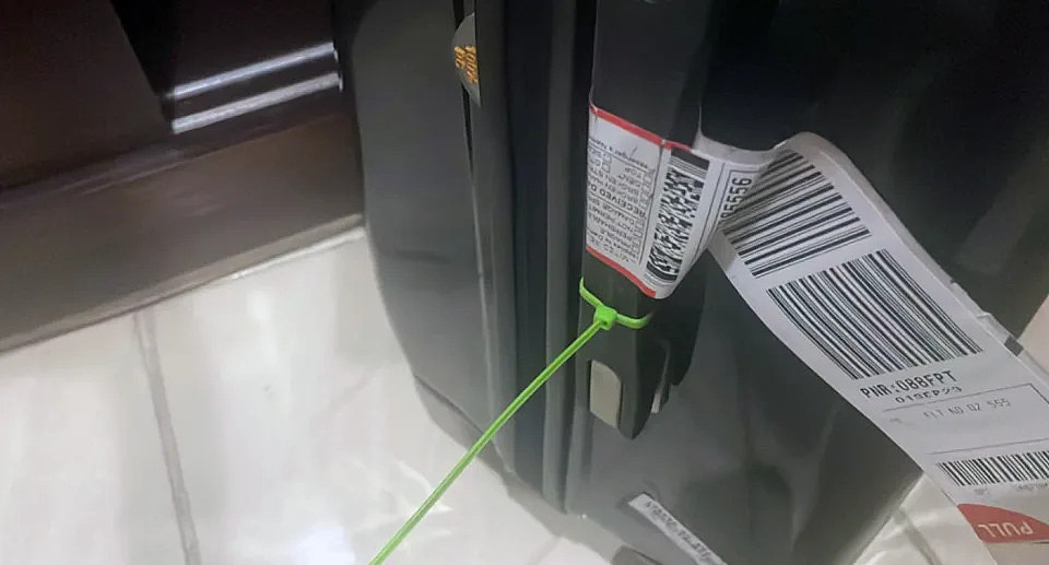 A green cable tie is seen strapped to a suitcase. 