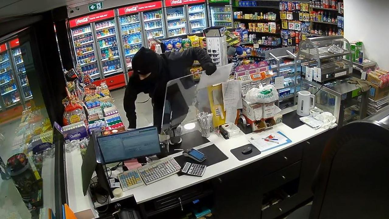 One of the youths climbs over the counter to steal cash.