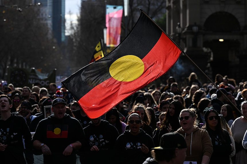 a large aboriginal flag flying above a large group of people at a city march